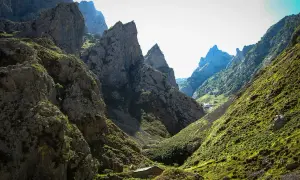 Kamienna chata w dolinie u stóp skalistych szczytów, przypominających kształtem **Naranjo de Bulnes**.