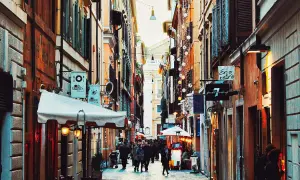 En livlig gränd i ett kvarter i Rom, med butiker och restauranger längs sidorna. Folk promenerar och njuter av atmosfären.