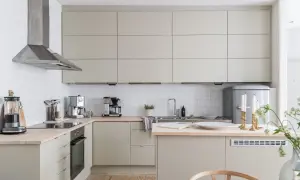Jasna, nowoczesna bezowa kuchnia z drewnianym blatem, stalowym okapem i białymi kafelkami. Widać ekspres do kawy, blender i lodówkę retro.