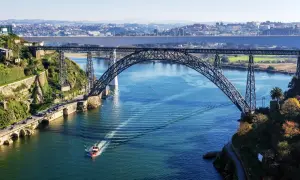 Majestatyczny porto most nad błękitną rzeką, z łodzią przecinającą fale i miastem w tle.