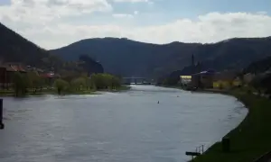 Flusslandschaft bei Ústí nad Labem mit bewaldeten Hügeln, Industriegebäuden und einer Stadt am Ufer.