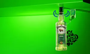 Butelka Żubrówki z trawą żubrową, 37,5% alkoholu. Obok kieliszek z zielonym płynem i napis "Go Wild".