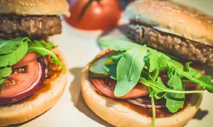 Dwa domowe hamburgery z bułką, kotletem, pomidorem, czerwoną cebulą i rukolą.