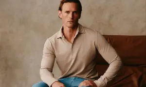 Ein Mann sitzt lässig in einem beigen Langarm-Polohemd, das an italienische Poloshirts für Herren erinnert.