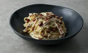 Porcja spaghetti carbonara z boczkiem i natką pietruszki w ciemnej misce.