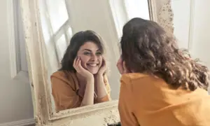 Donna sorride guardandosi allo specchio, un momento di riflessione sull'effetto specchio psicologia e sull'accettazione di sé.