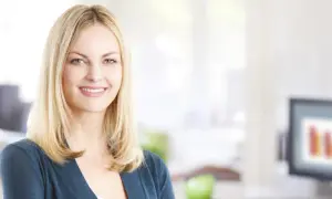 En leende kvinna med blont hår i en kontorsmiljö. Hon representerar effektiv kommunikation på arbetsplatsen.