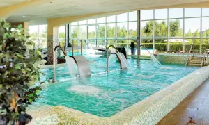 Piscina interior con cascadas de agua y vistas al exterior, ideal para una experiencia de spa relajante.