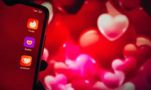 Na ekranie telefonu widać ikony aplikacji randkowych: Tinder, Badoo i W-Match. Tło to czerwone serca, symbolizujące miłość i poszukiwanie tej jedynej osoby. Wybór bezpiecznych portali randkowych to pierwszy krok do znalezienia szczęścia.