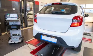 Controllo emissioni per la revisione microcar. Un'auto bianca è collegata a un analizzatore di gas di scarico in un'officina.