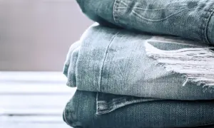 Stos znoszonego materiału na dżinsy, z widocznym przetarciem i strzępami.