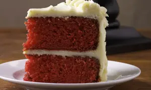 Ein Stück saftiger **red velvet** Kuchen mit cremiger Glasur auf einem weißen Teller.