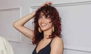 Donna sorridente con capelli castani mossi e tinta rossa, indossa orecchini dorati.