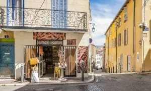 Bunte Häuser und ein Gewürzladen in der **Marseille Altstadt**. Eine schmale Gasse führt bergauf, gesäumt von sonnengelbem Mauerwerk und blauen Fensterläden.