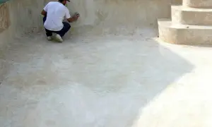 Hombre lijando la pared de una piscina vacía, preparándola para pintar cemento exterior.