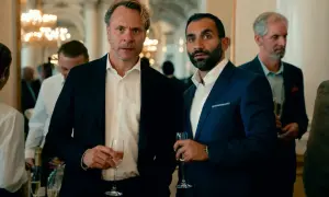 Två män i kostym med champagneglas i handen, en del av rollistan i Hundarna.