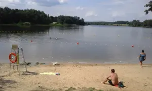 Słoneczny dzień nad rybnikiem zalew. Kąpielisko z bojami, ratownik na posterunku, plażowicze odpoczywają na piasku.
