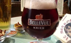 Szklanka piwa cherry Kriek Bellevue z pianką, obok jasne piwo i miseczki z przekąskami.