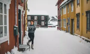 Uśmiechnięta kobieta w swetrze stoi na zaśnieżonej ulicy w Oslo zimą.