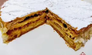 Una fetta di torta millefoglie con crema pasticcera e mandorle, cosparsa di zucchero a velo.
