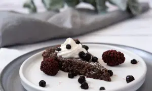 En bit vegansk kladdkaka med vispgrädde och bär.