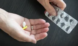 Dłoń trzyma białą i żółtą tabletkę. Obok puste opakowanie po lekach. Glicynian magnezu na co? Na stres i zmęczenie.