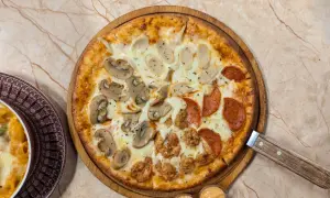 Pizza quattro stagioni avec champignons, saucisses, pepperoni et poulet frit. Une part de pâtes gratinées est visible à gauche.