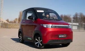 Czerwony, miejski pojazd elektryczny kategoria AM, z kobietą za kierownicą, zaparkowany na zewnątrz.