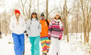 Cztery kobiety w zimowych kurtkach i kolorowych spodniach skiturowych damskich idą przez zaśnieżony las.