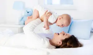 Szczęśliwa mama podrzuca dziecko, zastanawiając się, ile kosztuje opieka nad dzieckiem za godzinę.