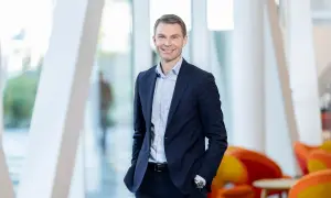 En leende man i mörkblå kostym, en del av Swedbank koncernledning, står framför ett modernt fönsterparti.