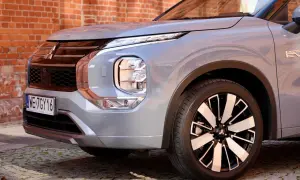 Przód srebrnego Mitsubishi Outlander 2025 z charakterystycznym grillem i reflektorami LED, zaparkowany na bruku przed ceglaną ścianą.