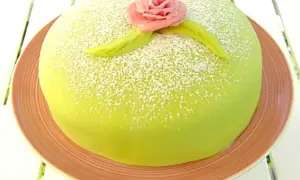 En vacker prinsesstårta med grön marsipan, pudrad med florsocker och dekorerad med en rosa ros. Perfekt för ett prinsesstårta recept!