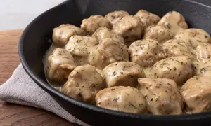 Pulpety w sosie śmietanowym, polane zieloną natką pietruszki, w czarnej patelni.
