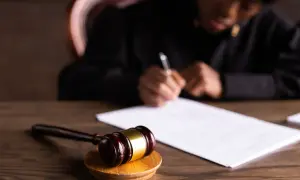 Młotek sędziowski i dokumenty na biurku. Referendarz sądowy pochyla się nad papierami, pisząc.