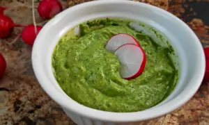 Zielone pesto z liści rzodkiewki w białej miseczce, ozdobione plasterkami rzodkiewki.