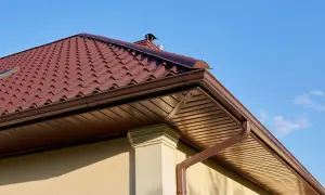 Brązowe, ciągnione rynny odprowadzają wodę z dachówki. Pod nimi widać drewniany sufit podwieszany.