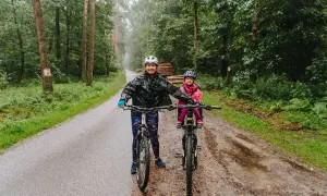 Mama i dziecko na rowerach w deszczu, odkrywają lasy kozłowieckie trasy rowerowe.