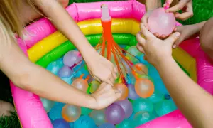 Manos infantiles llenando globos de agua en una piscina inflable multicolor. ¡Diversión garantizada con estos juegos de agua!