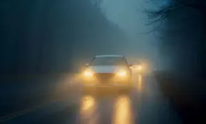 Voitures circulant dans le brouillard, leurs feux diurnes perçant la brume et illuminant la route mouillée par la pluie.