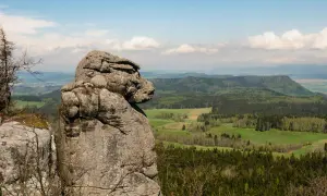 Skalna głowa spogląda na malownicze **góry stołowe**, gdzie leżą zielone doliny i lasy.