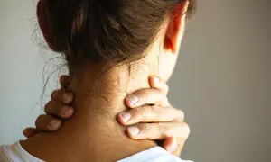 Frau greift sich an den Nacken, um einen steifen Nacken zu lindern. Was hilft sofort? Sanfte Dehnung und Wärme können Linderung bringen.