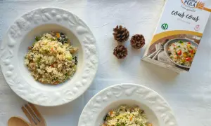 Piatti di cous cous con verdure e ceci, perfetti per le ricette cous cous invernale. Accanto, una confezione di cous cous e pigne decorative.