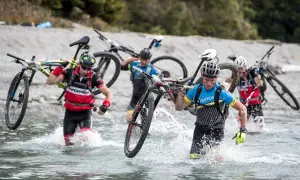 Teilnehmer eines **adventure racing** durchqueren mit Fahrrädern auf den Schultern einen Fluss.