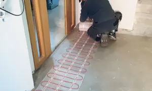 Instalator montuje ogrzewanie podłogowe elektryczne. Czerwone kable grzewcze na siatce czekają na przykrycie.