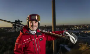 Ski-entusiast med skidor på axeln, klädd i röd jacka med SkiStar-logga. Han ser ut att vara en del av SkiStar ledning, redo för äventyr.