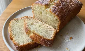 En saftig vegansk sockerkaka, pudrad med florsocker, ligger på en tallrik. Två skivor är upplagda bredvid.