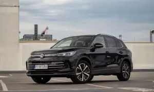 Czarny Volkswagen Tiguan na parkingu. W tle budynki i dźwig. Wiele osób szuka volkswagen tiguan opinie przed zakupem.