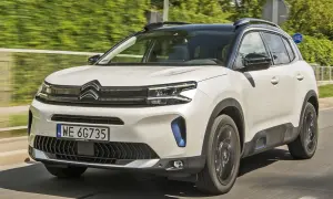 Biały Citroen C5 Aircross 2025 z czarnym dachem pędzi po drodze, otoczony zielenią.