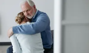 Starszy mężczyzna obejmuje pogrążoną w smutku kobietę. Wsparcie w trudnych chwilach, jak poradzić sobie ze śmiercią mamy.